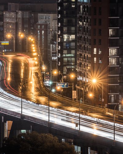 Glowing light streaks from a wet Gardiner Expressway as traffic never stops.  Hot & rainy, muggy summer night in Lakeside Toronto Ontario, Canada.